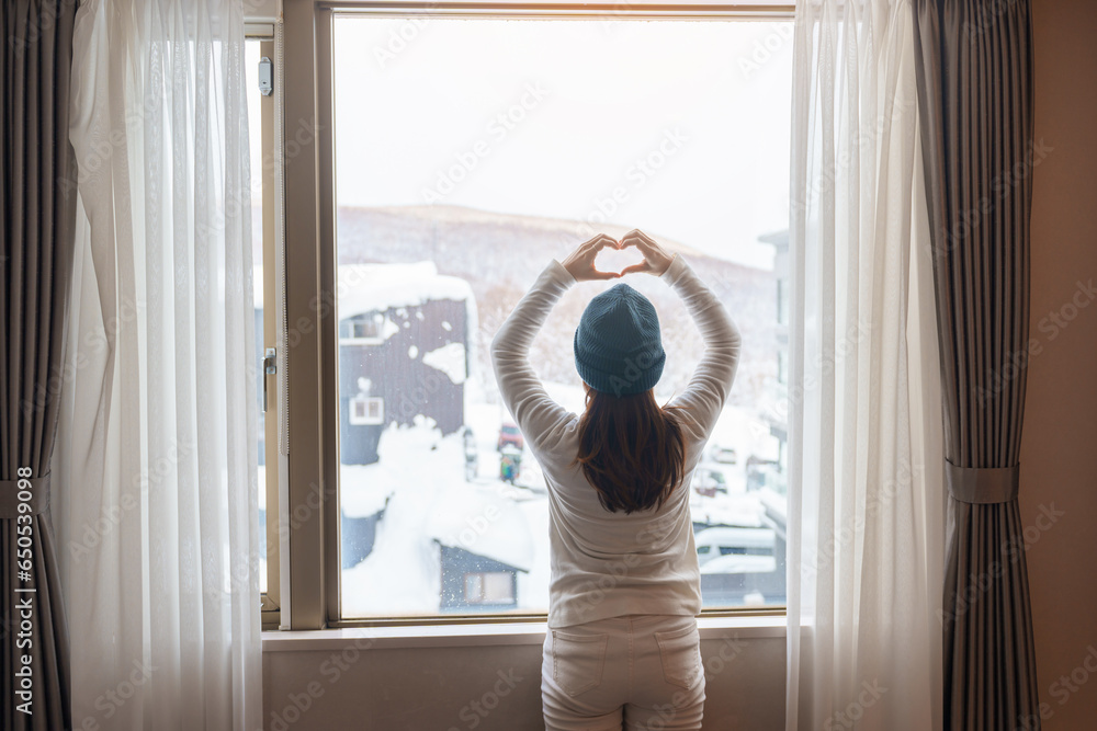 young woman in sweater looking through the window in winter season, happy female rising arms and stretching after waking at apartment or home in the morning. Lifestyle and Relaxing concepts young woman in sweater looking through the window in winter season, happy female rising arms and stretching after waking at apartment or home in the morning. Lifestyle and Relaxing concepts