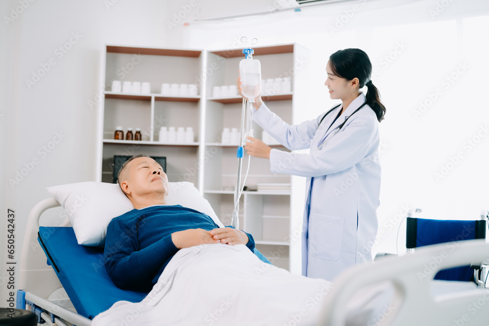Asian doctor in white suit take notes while discussing and Asian elderly, man patient who lying on bed with receiving saline solution in hospital . Asian doctor in white suit take notes while discussing and Asian elderly, man patient who lying on bed with receiving saline solution in hospital .