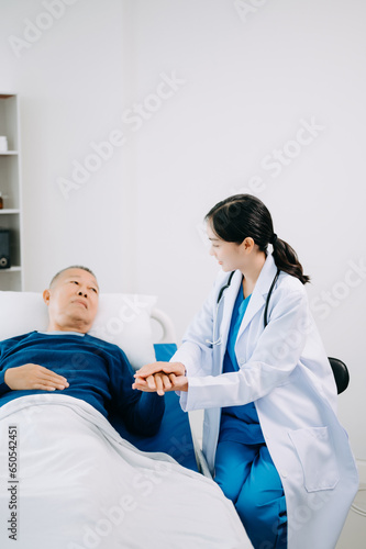 Asian doctor in white suit take notes while discussing and Asian elderly  man patient who lying on bed with receiving saline solution in hospital .