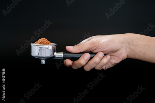 Close-up of hand holding a portafilter with ground coffee