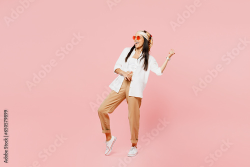 Full body young musician singer latin woman she wear white shirt casual clothes sunglasses pretend playing guitar with hand gesture isolated on plain pastel pink background studio. Lifestyle concept. photo