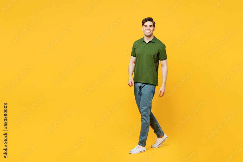 Full body side view young caucasian smiling happy man he wears green t-shirt casual clothes walking going strolling look camera isolated on plain yellow background studio portrait. Lifestyle concept. Full body side view young caucasian smiling happy man he wears green t-shirt casual clothes walking going strolling look camera isolated on plain yellow background studio portrait. Lifestyle concept.