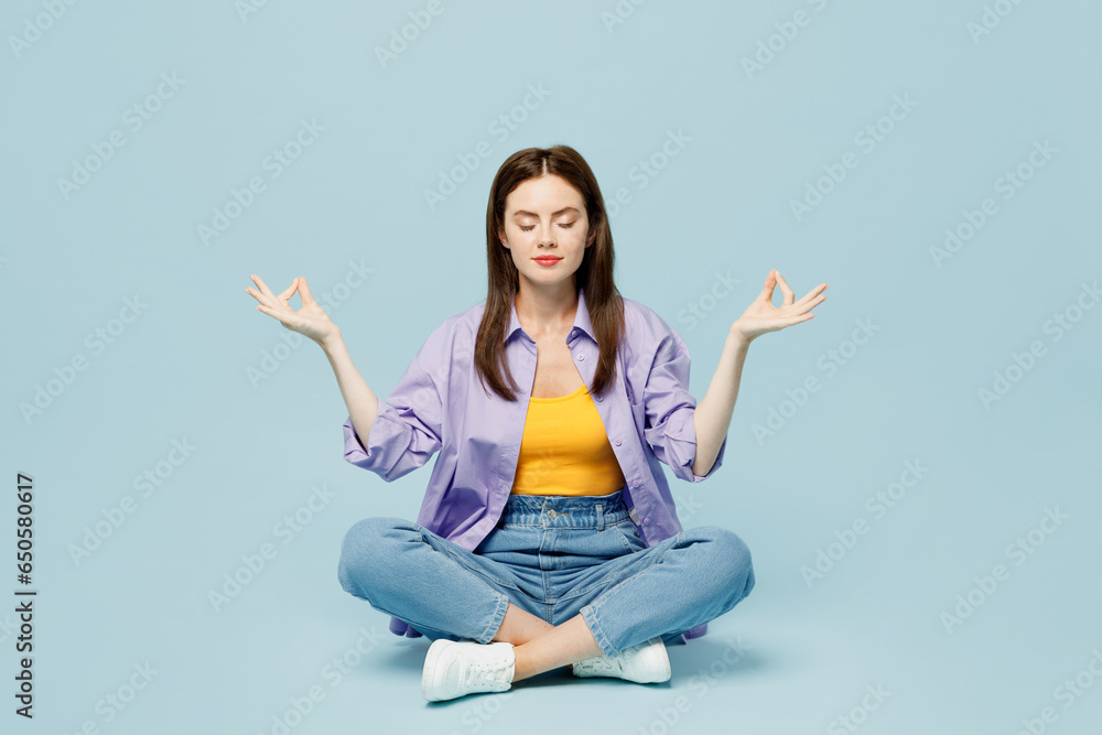 Φωτογραφία Full body young happy woman wears purple shirt yellow t-shirt casual clothes sit hold spread hands in yoga om aum gesture relax meditate try calm down isolated on plain pastel light blue background