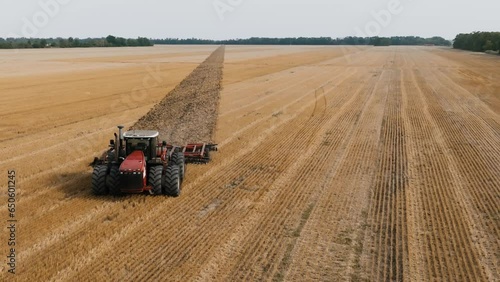 Big red Tractor Pulling Disc Harrow Through Field in Preparation soil for Planting new crops, Agriculture. Aerial view of tractor plowing the field. slow motion video.