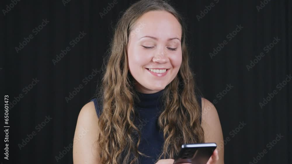 Attractive woman in smiles texting tapping on phone against black background Attractive woman in smiles texting tapping on phone against black background