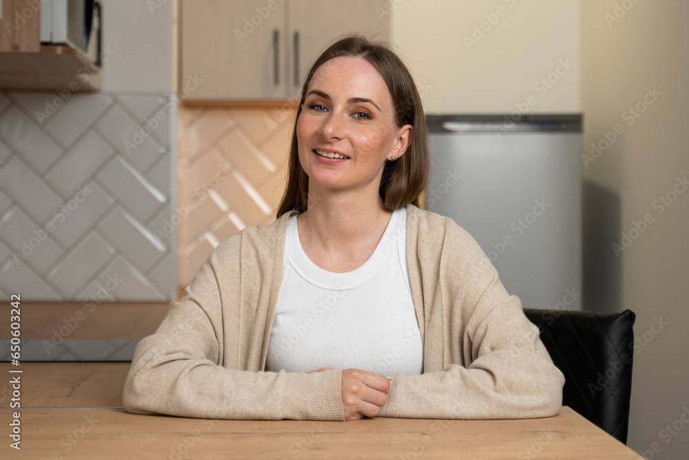 Smiling young blogger, sitting at home in the kitchen, talking, looking at the camera, talking in a video chat, conference call, recording a video blog. Smiling young blogger, sitting at home in the kitchen, talking, looking at the camera, talking in a video chat, conference call, recording a video blog.