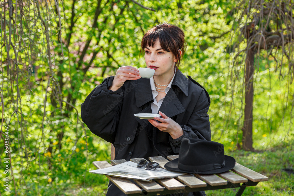 A beautiful girl drinks coffee at the table, in a raincoat, in a white shirt, in black trousers with suspenders A beautiful girl drinks coffee at the table, in a raincoat, in a white shirt, in black trousers with suspenders