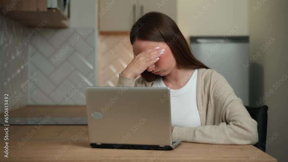 The concept of remote work, business and people is a tense or tired young woman with a laptop computer working in a home office in the kitchen. The concept of remote work, business and people is a tense or tired young woman with a laptop computer working in a home office in the kitchen.