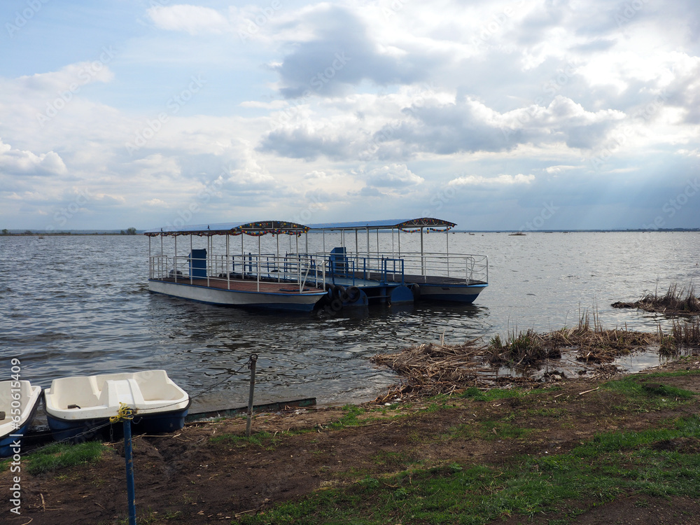 Spring landscape with catamaran and water bikes on the shore of a large lake, against a clear sky. Rural landscape, a beautiful place to relax.