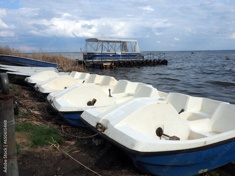 Spring landscape with catamaran and water bikes on the shore of a large lake, against a clear sky. Rural landscape, a beautiful place to relax.