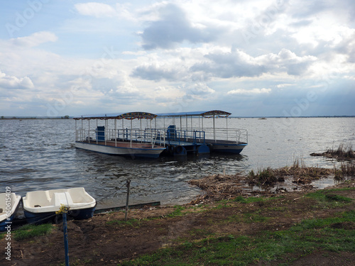 Obraz na płótnie Spring landscape with catamaran and water bikes on the shore of a large lake, against a clear sky. Rural landscape, a beautiful place to relax. w salonie