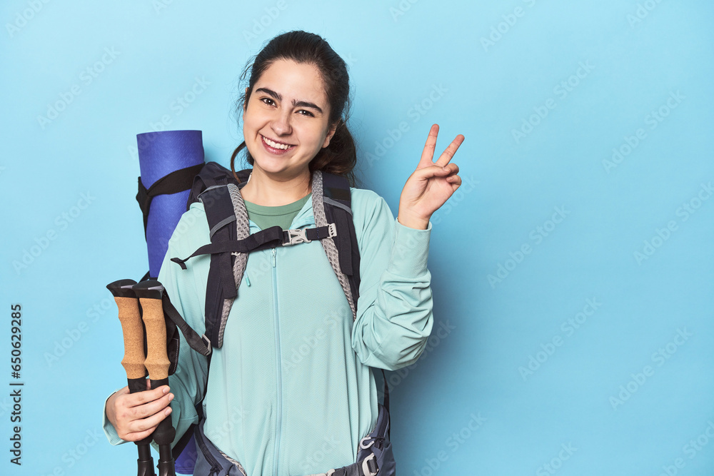 Hiker with backpack and poles on blue showing number two with fingers. Hiker with backpack and poles on blue showing number two with fingers.