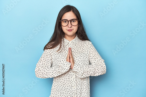 Foto Young Caucasian woman on blue backdrop praying, showing devotion, religious person looking for divine inspiration