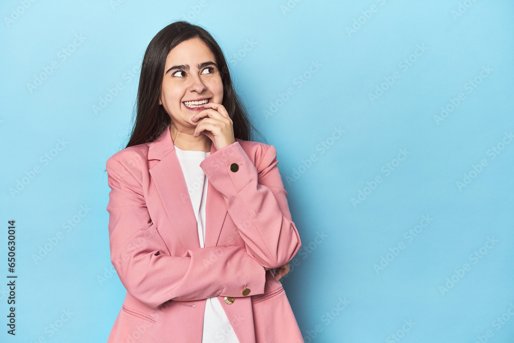 Young Caucasian woman on blue backdrop relaxed thinking about something looking at a copy space. Young Caucasian woman on blue backdrop relaxed thinking about something looking at a copy space.