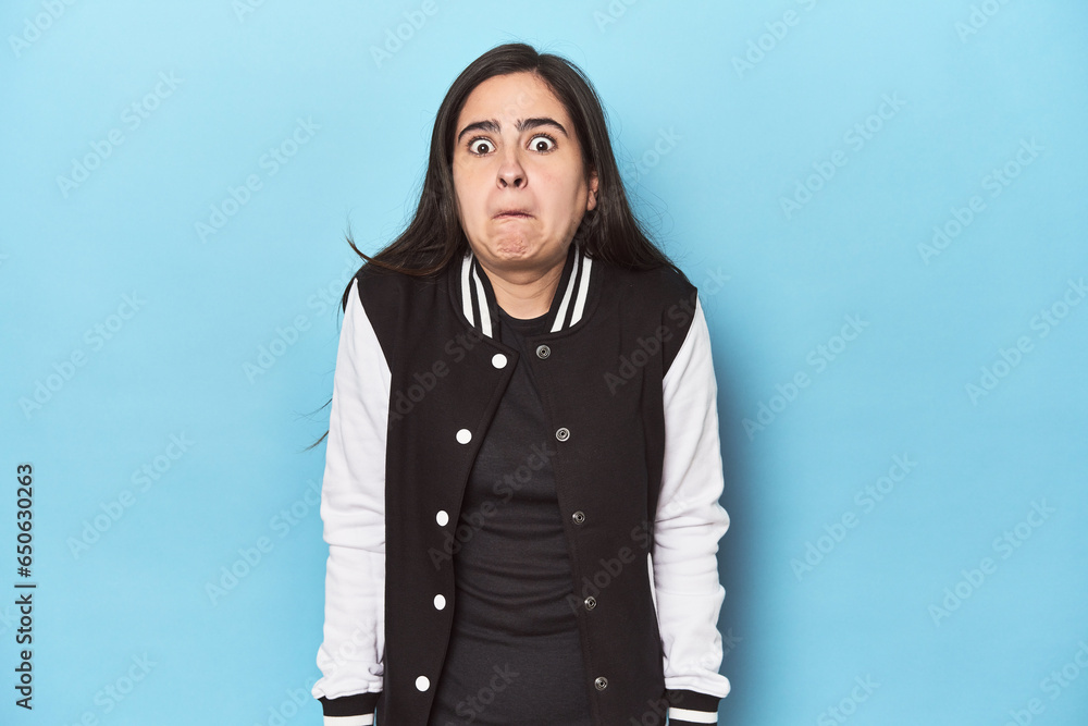 Young Caucasian woman on blue backdrop shrugs shoulders and open eyes confused. Young Caucasian woman on blue backdrop shrugs shoulders and open eyes confused.