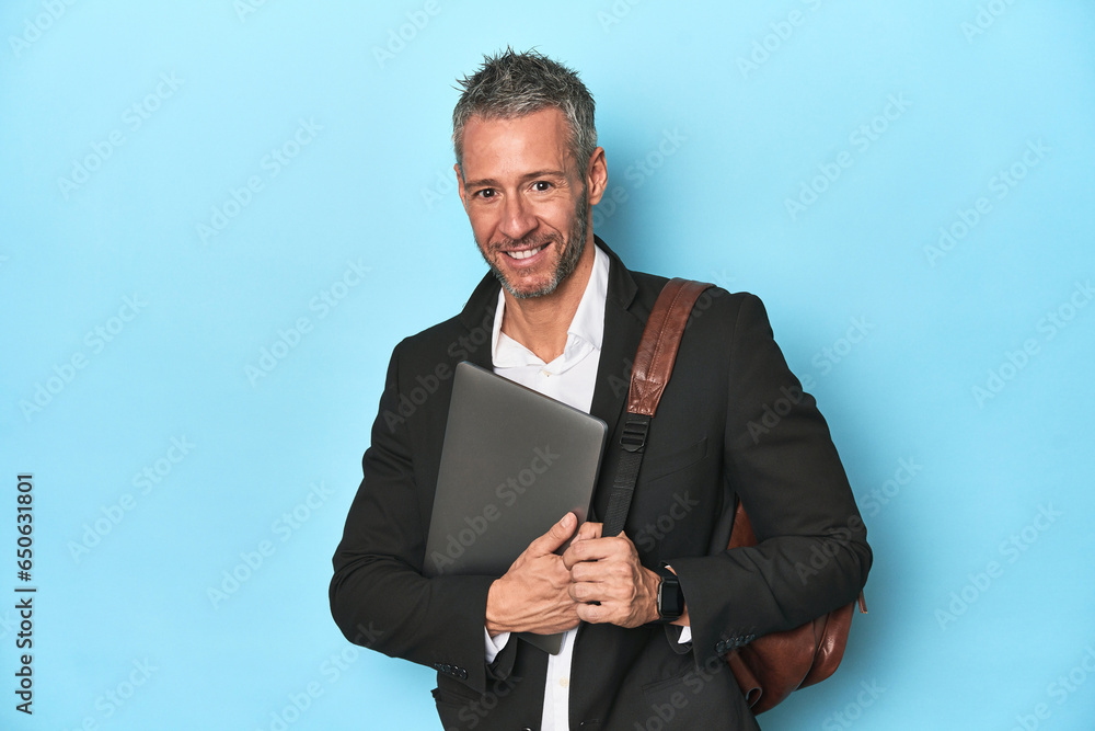 Businessman with backpack holding laptop on blue backdrop Businessman with backpack holding laptop on blue backdrop