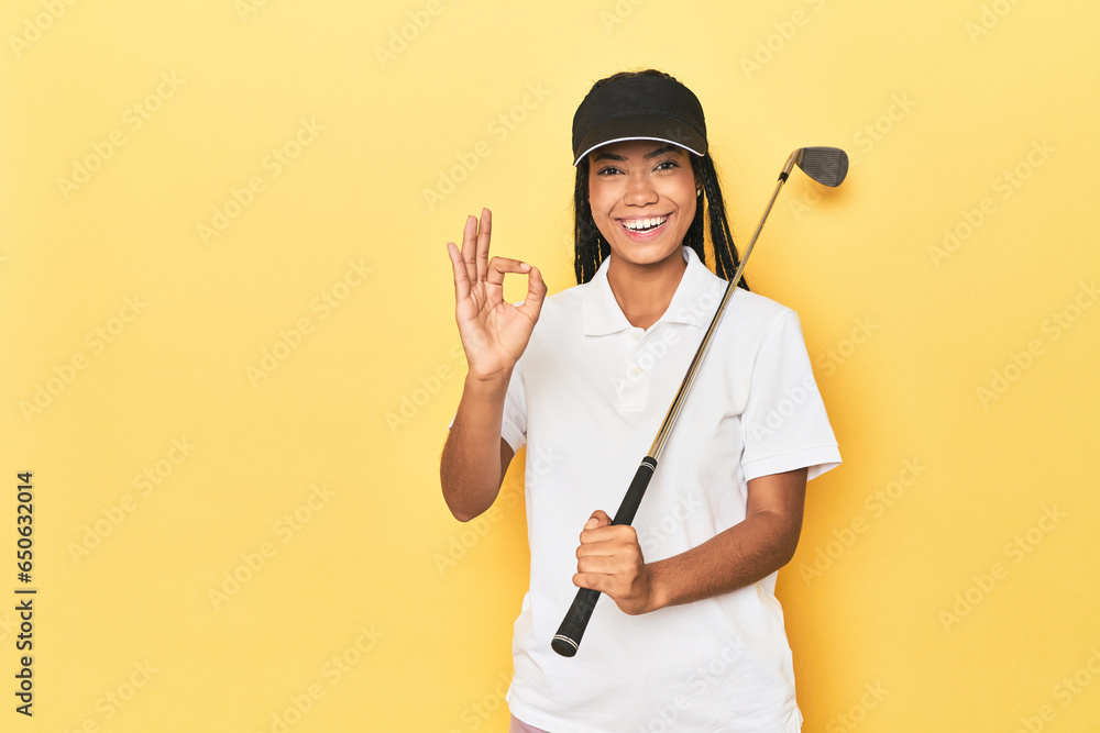 Indonesian female golfer on yellow backdrop cheerful and confident showing ok gesture. Indonesian female golfer on yellow backdrop cheerful and confident showing ok gesture.
