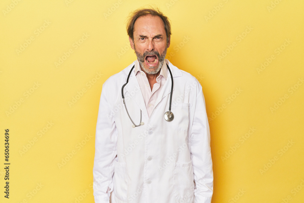 Doctor with stethoscope in yellow studio screaming very angry and aggressive. Doctor with stethoscope in yellow studio screaming very angry and aggressive.