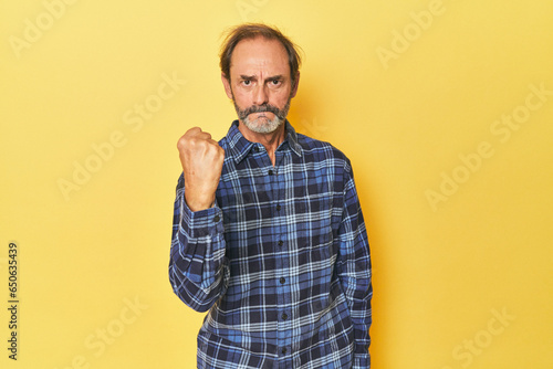 Bilde på lerret Caucasian middle-aged man in yellow studio showing fist to camera, aggressive facial expression