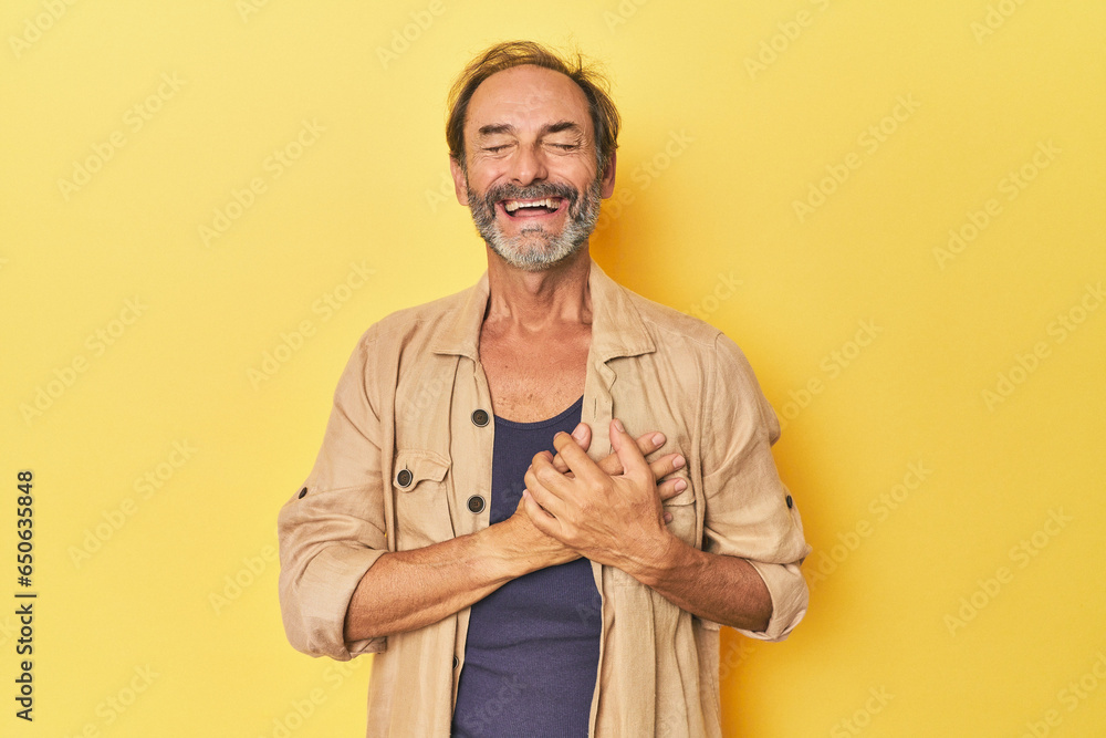 Caucasian middle-aged man in yellow studio laughing keeping hands on heart, concept of happiness. Caucasian middle-aged man in yellow studio laughing keeping hands on heart, concept of happiness.