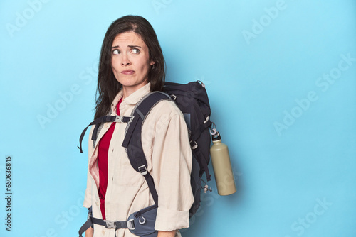 Billede på lærred Adventurous woman with backpack on blue confused, feels doubtful and unsure