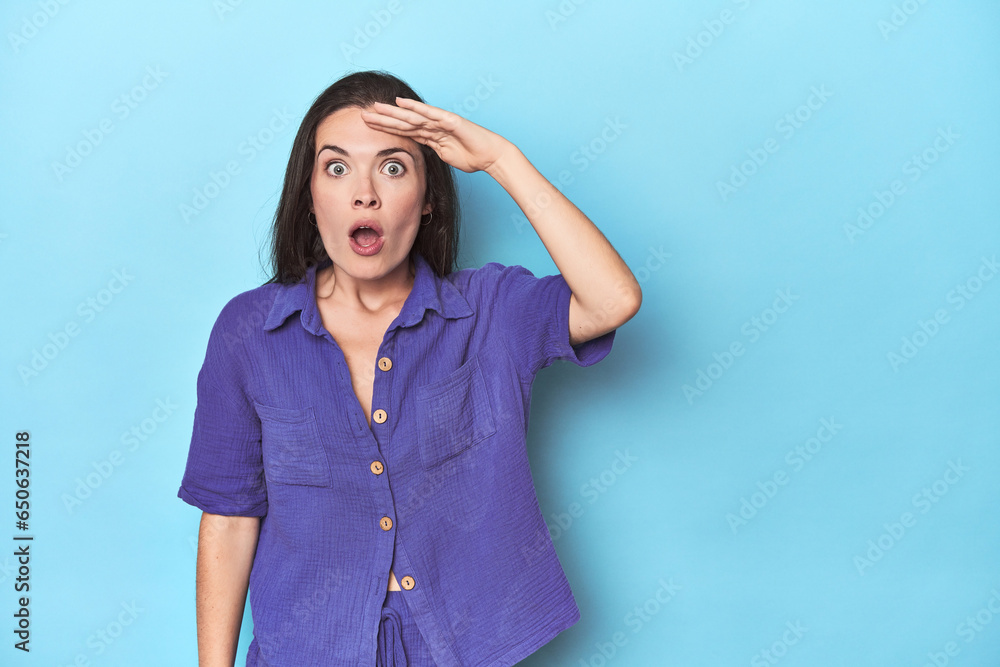 Young caucasian woman on blue backdrop shouts loud, keeps eyes opened and hands tense. Young caucasian woman on blue backdrop shouts loud, keeps eyes opened and hands tense.