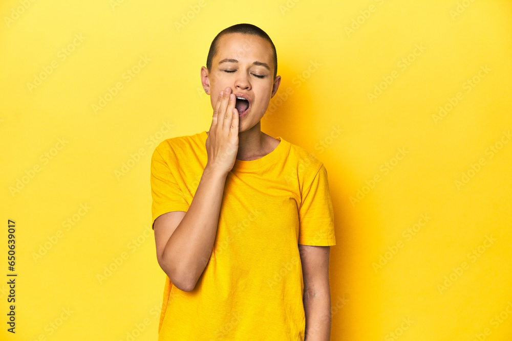 Young woman in yellow tee, yellow studio backdrop yawning showing a tired gesture covering mouth with hand. Young woman in yellow tee, yellow studio backdrop yawning showing a tired gesture covering mouth with hand.