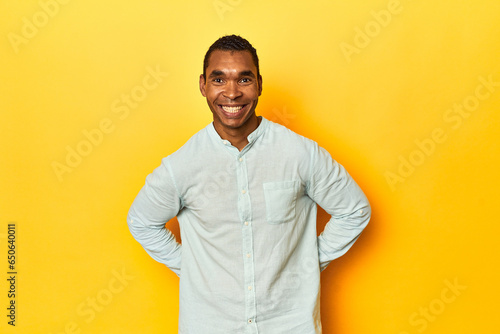 African American man in blue shirt, yellow studio, happy, smiling and cheerful.