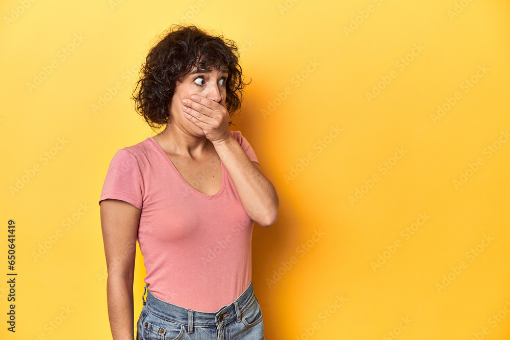 Curly-haired Caucasian woman in pink t-shirt thoughtful looking to a copy space covering mouth with hand. Curly-haired Caucasian woman in pink t-shirt thoughtful looking to a copy space covering mouth with hand.