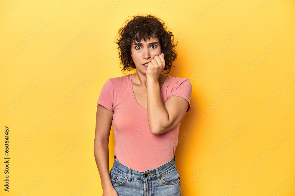 Curly-haired Caucasian woman in pink t-shirt biting fingernails, nervous and very anxious. Curly-haired Caucasian woman in pink t-shirt biting fingernails, nervous and very anxious.