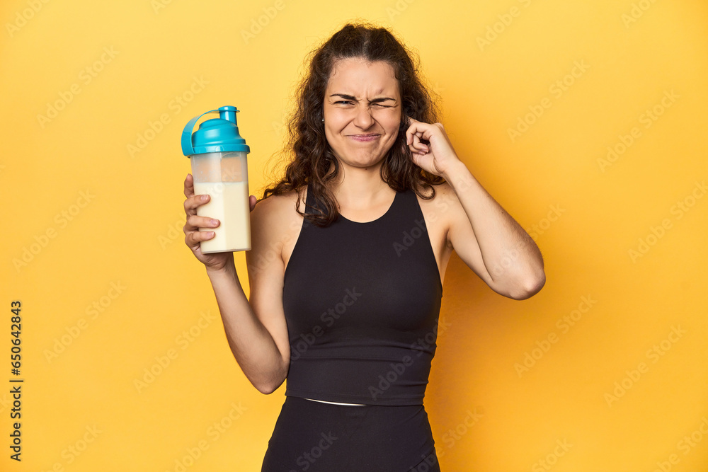 Woman holding a protein shake, in sportswear, covering ears with hands. Woman holding a protein shake, in sportswear, covering ears with hands.