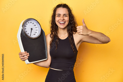 Young Caucasian woman with scale, weight management concept, yellow background. photo
