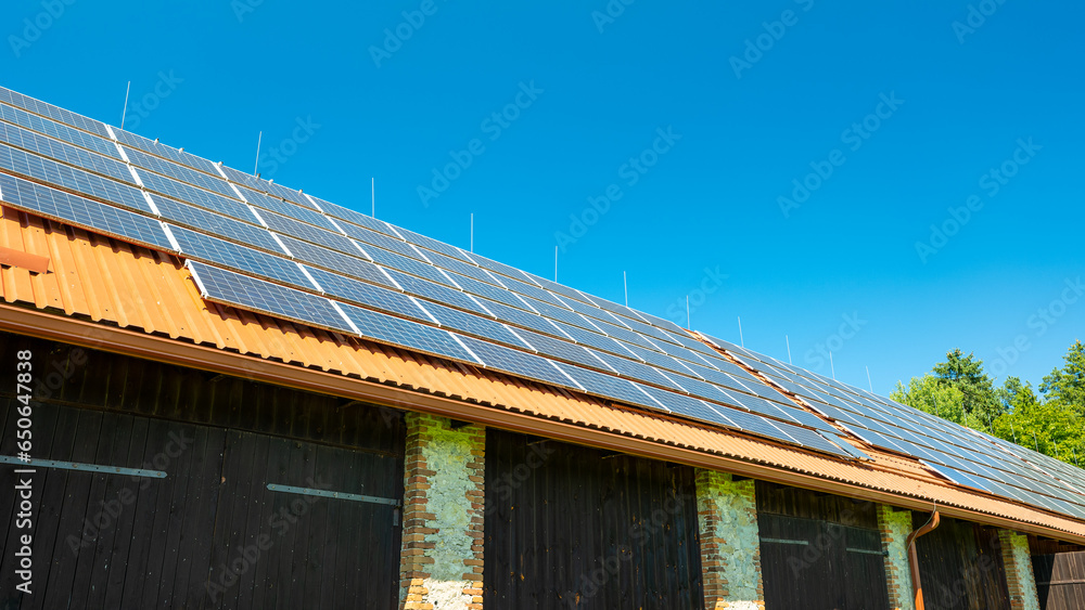Big brick barn on a farm. Solar panels installed on the roof of the barn. .The roof is covered with red trapezoidal sheet metal