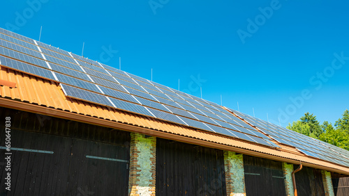 Obraz na płótnie Big brick barn on a farm. Solar panels installed on the roof of the barn. .The roof is covered with red trapezoidal sheet metal w salonie