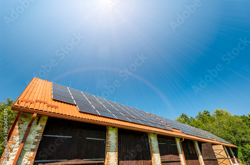 Big brick barn on a farm. Solar panels installed on the roof of the barn. The roof is covered with red trapezoidal sheet metal photo