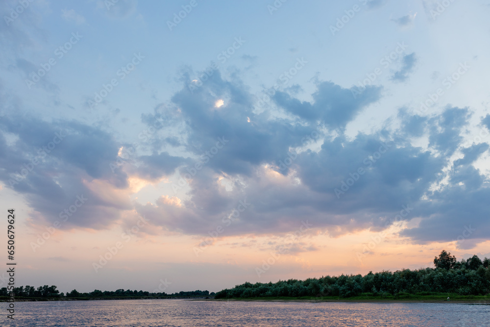 Beautiful sky over the river with fluffy blue clouds and orange sun at sunset. Dawn on the lake. Picturesque sky at sunrise