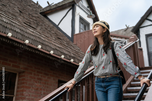 happy asian Japanese female traveler enjoying looking at the exterior of country house on the wooden staircase while exploring solvang Danish village in California usa