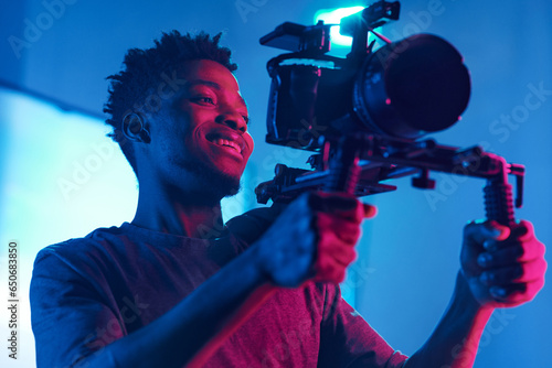фотографія Young African American cameraman shooting with professional camera in studio