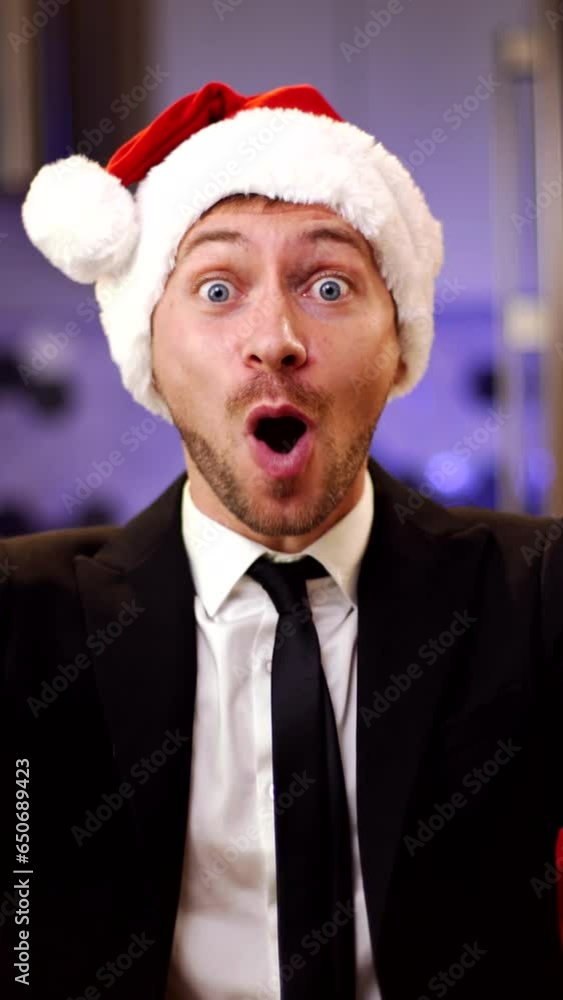 Young businessman in red christmas santa hat very happy and rejoices sitting on the couch. Christmas sales concept. Vertical video. Young businessman in red christmas santa hat very happy and rejoices sitting on the couch. Christmas sales concept. Vertical video.