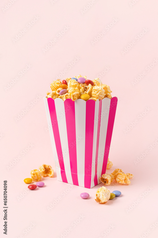 Tasty sweet popcorn with dragee candies in striped bucket on pink background