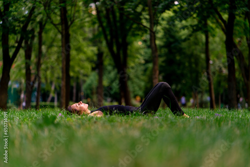 Active beautiful yogi woman resting in the city park after training lying on a fitness mat looking at the sky