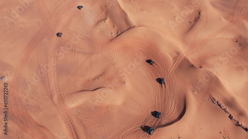 A drone flies over a caravan of buggies driving through the desert sand