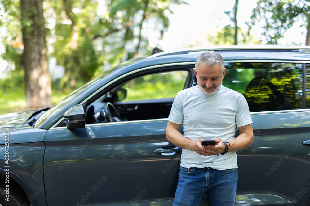 Mid adult man text messaging on smartphone while standing next to his car