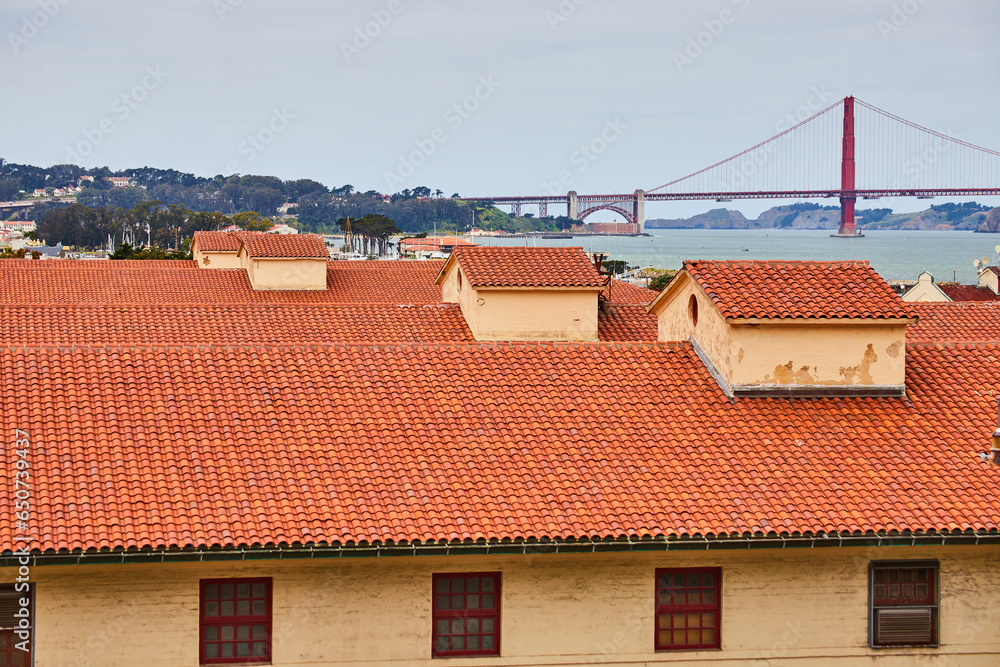 Yellow building with red trim around windows and orange clay shingle roofs with Golden Gate Bridge Yellow building with red trim around windows and orange clay shingle roofs with Golden Gate Bridge