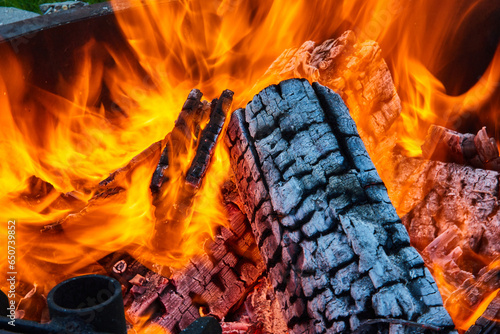 Canvas Print Intense flames surrounding logs inside round fire pit with exposed white ashen l