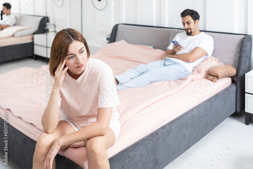 Frustrated and depressed woman sitting on the edge of the bed after conflict with her husband because of his erectile dysfunction problem