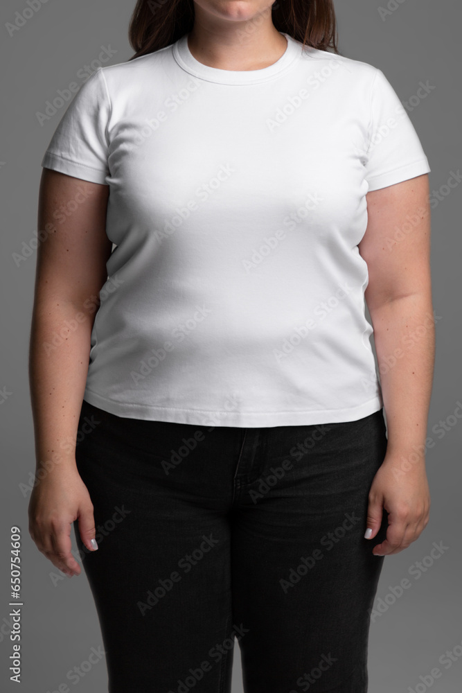 Plus size model on grey background with no face. Young female in blank white t-shirt front view. Design women t shirt template and mock-up for branding or print. Plus size model on grey background with no face. Young female in blank white t-shirt front view. Design women t shirt template and mock-up for branding or print.