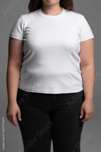 Plus size model on grey background with no face. Young female in blank white t-shirt front view. Design women t shirt template and mock-up for branding or print.
