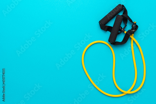 Minimalist flat lay photo of resistance band with handles over turquoise blue background. Top view of yellow fitness resistance band with handles with copy space.