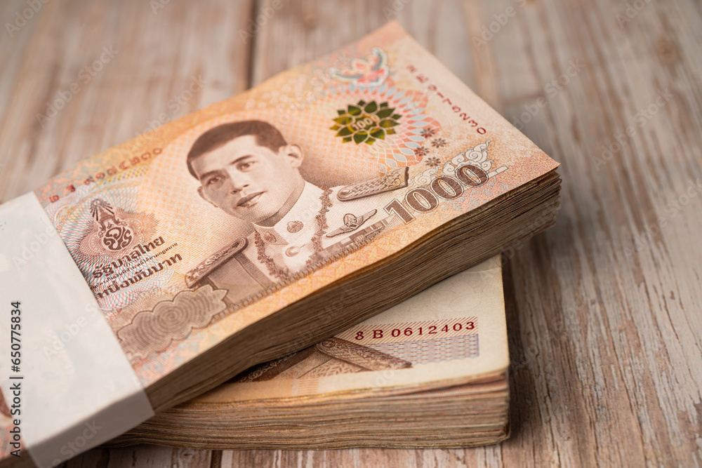 Fototapeta premium Stack of Thai baht banknotes on wooden background, business saving finance investment concept.